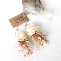 two pairs of earrings with flowers and feathers attached to the earwires on a white surface