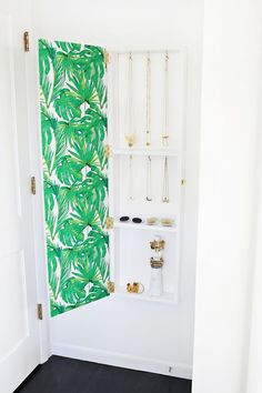 a white bathroom with green wallpaper and gold jewelry hanging on the shower stall door