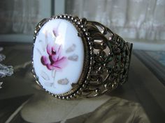 A beautifully ornate gold washed floral filigree painted glass rose cameo hinged bangle bracelet. The cameo measures 1 5/8'' x almost 1 1/4''. The bracelet measures 1 7/8'' at the widest. Also measures 2 1/2'' x 2 1/8'' across, and 7 5/8'' along the inside. In very good condition with subtle subduing of the gold. revealing the cool shiny silver underneath. Cameo Bracelet, Floral Filigree, Filigree Bracelet, Glass Rose, Vintage Cameo, Gold Wash, Hinged Bangle, Painted Glass, Shiny Silver