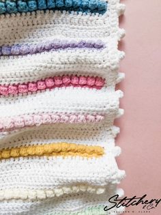 a crocheted blanket with multicolored stripes on it sitting on top of a pink surface