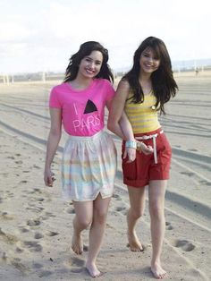 two young women walking on the beach with their hands in each other's pockets