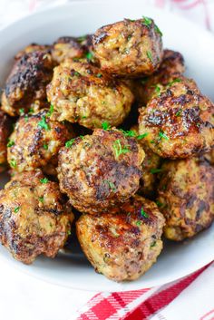 a white bowl filled with meatballs on top of a red and white checkered table cloth