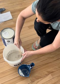 a woman kneeling down on the floor next to two buckets of paint and a cup