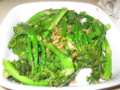 a white plate topped with broccoli covered in nuts and green beans on top of a table