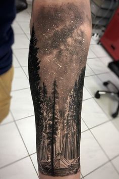 a man's arm with a forest scene and stars in the sky on it