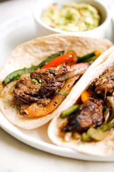 two steak fajitas on a plate with guacamole and salsa