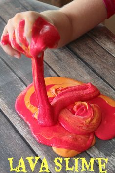 a child's hand holding a red and yellow cake with icing on it