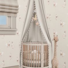 a giraffe standing next to a baby crib in a room with wallpaper