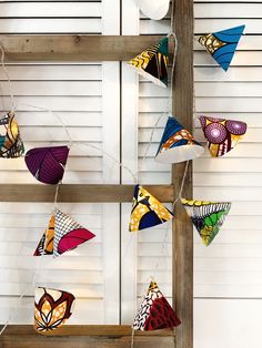 several colorful kites hanging from the side of a wooden ladder in front of a white wall