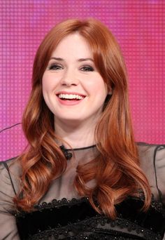 a woman with long red hair smiling and wearing a black dress on the set of her show