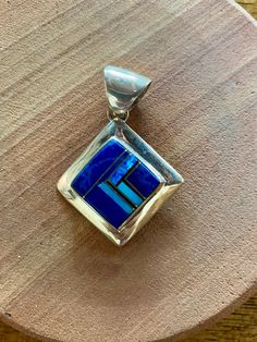 This beautifully well crafted Square Pendant has been handmade by a Navajo Artisan. The Colors of the Pendant come from Lapis Lazuli, Turquoise and Blue Opal. It is stamped Sterling and signed by the Artist. The Pendant measures 1.75” long and over 1.25” wide. There are two pendants available and the design will vary. “Winds of Wisdom” (Lapis Lazuli, Turquoise and Blue Opal. The Navajo (Dine’) believe that the wind is a powerful source. The native tradition believes that at any moment, the blowi Artisan Blue Jewelry With Inlay, Traditional Blue Inlay Jewelry, Traditional Blue Jewelry With Inlay, Handmade Southwestern Blue Jewelry, Blue Bohemian Jewelry With Inlay, Artisan Blue Rectangular Jewelry, Square Pendant, Blue Opal, Turquoise Blue