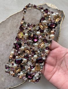 a hand holding a cell phone case covered in pearls and swarong crystals on a marble slab