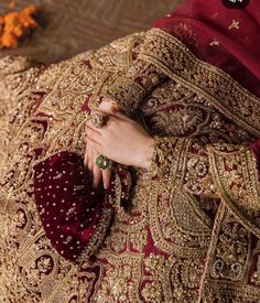 a woman in a red and gold wedding dress with her hands on her chest, wearing an elaborate ring