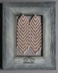 two brown and white chevroned earrings hanging from a gray framed photo in a frame