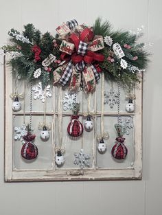 an old window decorated for christmas with ornaments and bows on the windowsill is hung in front of a white wall