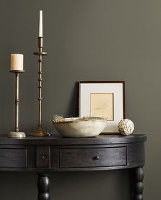 a wooden table with a bowl and two candles on it next to a framed photograph