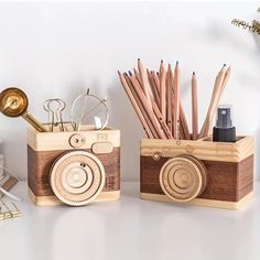 two wooden boxes with pencils, pens and an analog camera on them sitting on a table