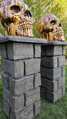 two cement skulls sitting on top of each other in front of some grass and trees