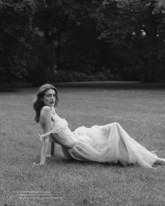 a woman laying on the ground in a field wearing a long white dress and heels