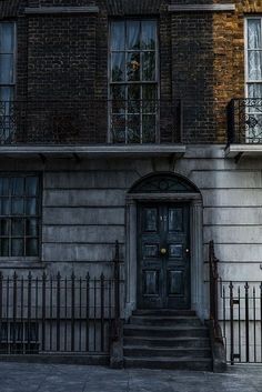 an old brick building with wrought iron railings and a clock on the front door