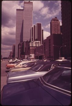 many cars parked in a lot with tall buildings behind them