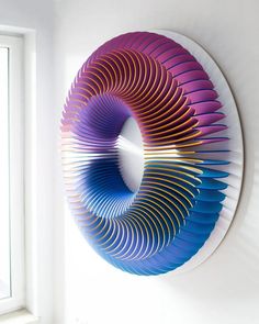 a colorful sculpture is hanging on the wall next to a window with a white frame