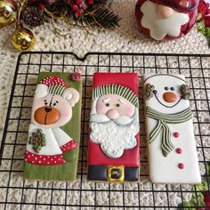 three decorated cookies sitting on top of a wire rack next to christmas decorations and ornaments