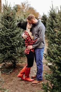 a man and woman standing next to each other in the middle of a christmas tree farm