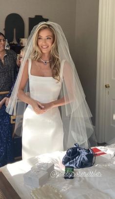 a woman standing in front of a bed wearing a white wedding dress with a veil