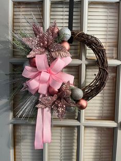 a wreath hanging on the side of a door with pink ribbon and ornaments around it