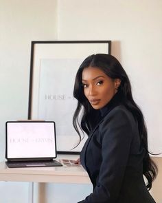 a woman sitting at a desk with a laptop in front of her, she is wearing a black blazer and pants