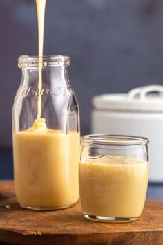 a glass jar filled with yellow liquid next to a container full of orange juice on a wooden cutting board