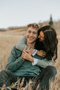 a man and woman sitting on the ground hugging each other in a field with tall grass