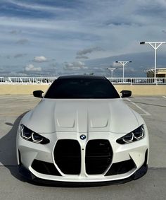 the front end of a white car parked in a parking lot with blue sky and clouds