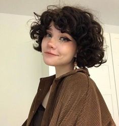 a close up of a person wearing a brown sweater and black pants with curly hair