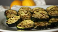 grilled zucchini on a white plate with oranges in the background