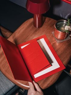 a person holding an open book on top of a wooden table next to a plant