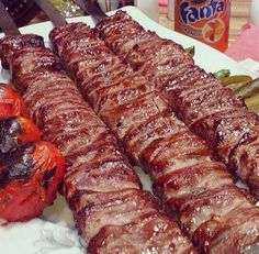 several skewered meats and vegetables on a white plate next to cans of soda