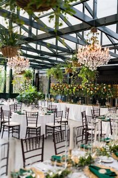 an indoor wedding venue set up with tables and chairs, chandeliers and greenery