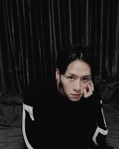 a young man sitting on top of a bed next to a black curtained wall