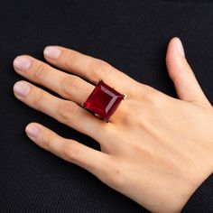 a woman's hand wearing a ring with a large red stone on the middle