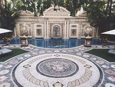 an elaborately designed pool in the middle of a garden with lounge chairs and umbrellas