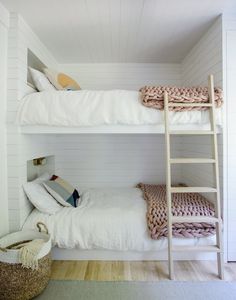 two bunk beds in a room with white walls and wood flooring, one has a ladder that leads to the second bed