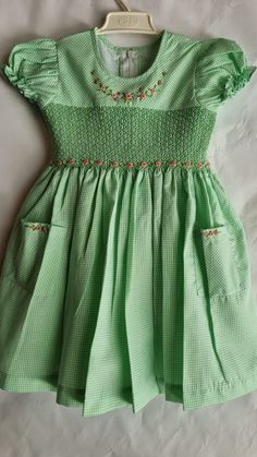 "This dress is smocked with matching green color and beautiful hand embroidered roses added around the neckline and on the smocking. The skirt comes with matching pockets, with same detailed hand embroidered roses.   Dress is fully lined with matching soft cotton material. The back closes with a zip and tie sashes. Material Outer fabric - Polycotton Inner fabric -100% Cotton  Instructions Cold gentle hand wash Available sizes, Size 3-6 months (AU 00) Length 14\" Chest circumference 20\" Size 6-12 months (AU 0) Length 16\" Chest circumference 21\" Size 1  (12-18 months) Length 18\" Chest circumference 22\" Size 2 (18-24 months) Length 20\" Chest circumference 23\" Size 3 Length 22\"  Chest circumference 24\" Size 4  Length 24\"  Chest circumference 25\" Size 5   Length 26\"  Chest circumfer Fitted Gingham Smocked Dress With Short Sleeves, Gingham Short Sleeve Dress With Smocked Bodice, Short Sleeve Gingham Dress With Smocked Bodice, Gingham Dress With Smocked Bodice And Short Sleeves, Fitted Green Dress With Smocked Back, Gingham Dress With Smocked Bodice For Garden Party, Short Sleeve Gingham Smock Dress, Short Sleeve Gingham Smocked Dress, Gingham Dress With Smocked Back For Garden Party