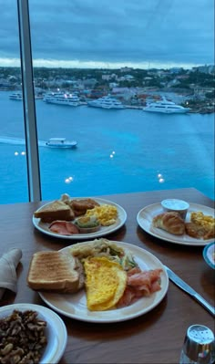 plates of food are on a table overlooking the water and boats in the bay behind them