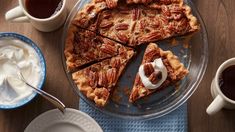 a pecan pie on a plate with two cups of coffee