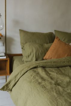 a bed with green linens and pillows in a white room next to a nightstand