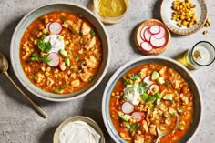 two bowls filled with soup and vegetables next to glasses of beer, spoons and napkins