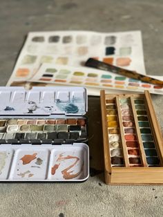 an assortment of art supplies including watercolors, paintbrushes and paper on the ground