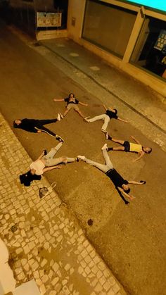 five people laying on the ground in front of a building with their arms around each other